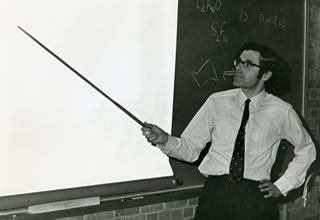 a black and white image of a man pointing a large pointer at a white board