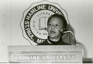 A black and white image of an unidentified woman speaking at a Hamline University podium