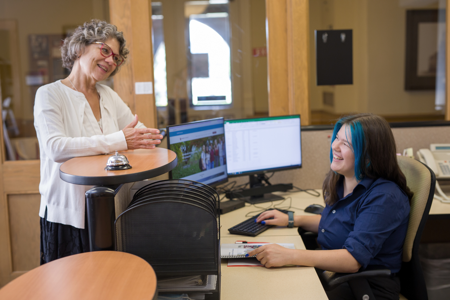 Student manning desk, talking to professor, student job