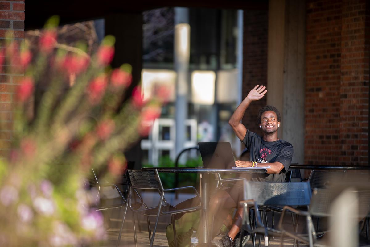 A Hamline student waving from a table