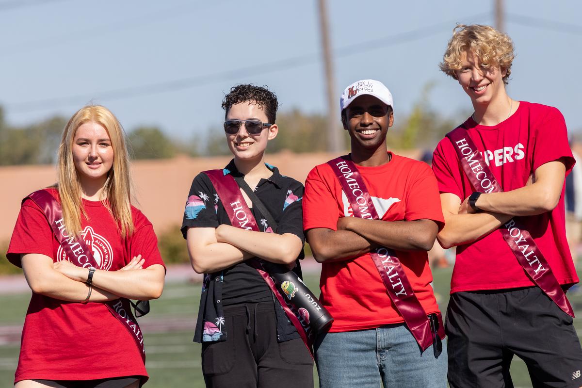 Four Hamline students wearing Hamline gear and posing on a field