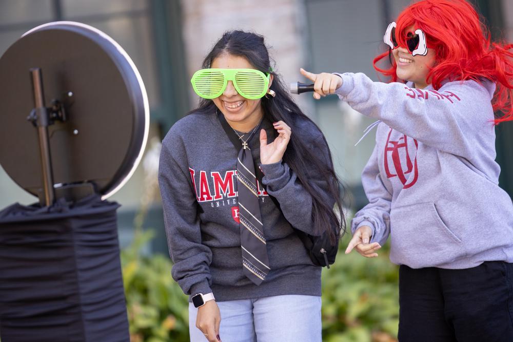 Two students wearing wigs and huge sunglasses at a photo stand