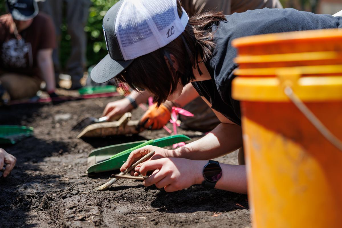 Anthropology students leaning in and brushing dirt off of artifacts during a dig