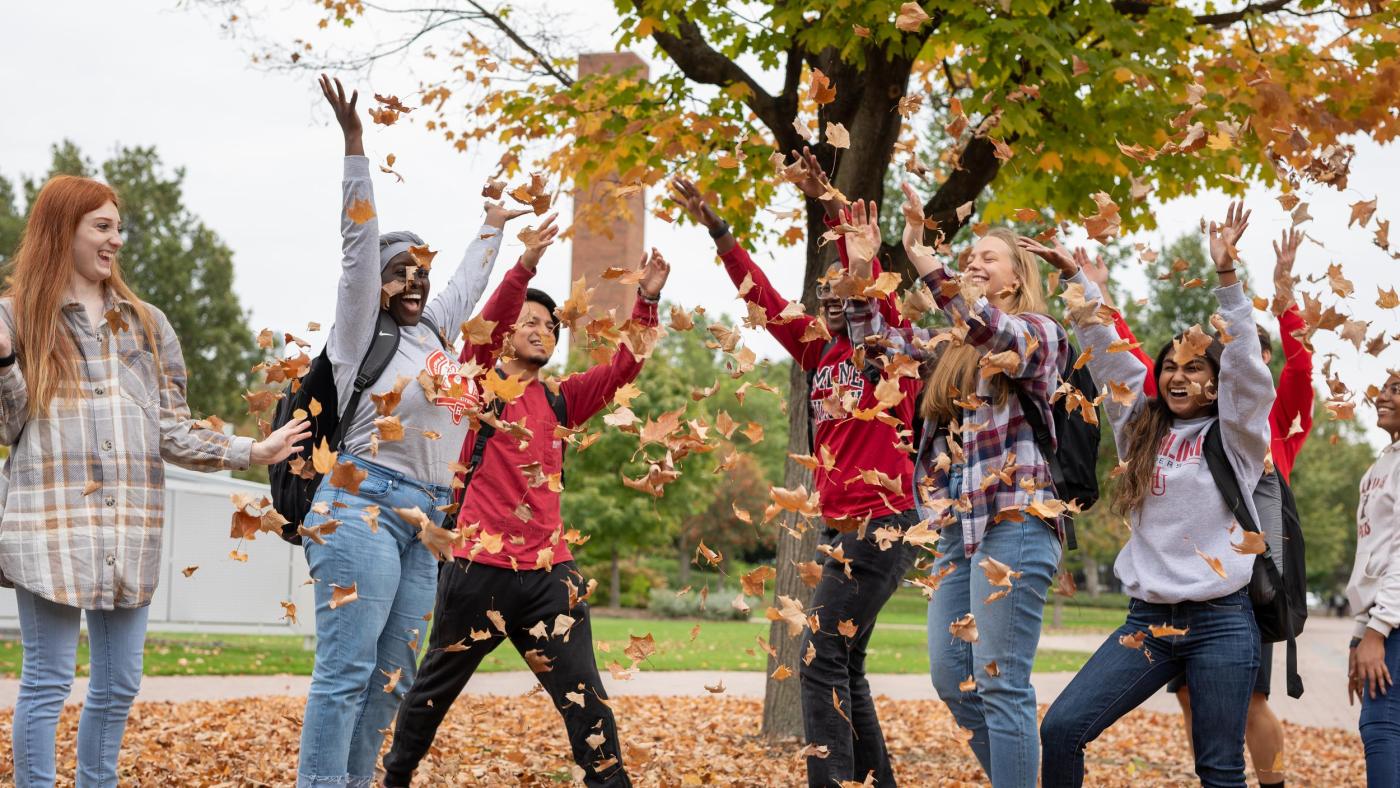 A group of students throwing fall leaves