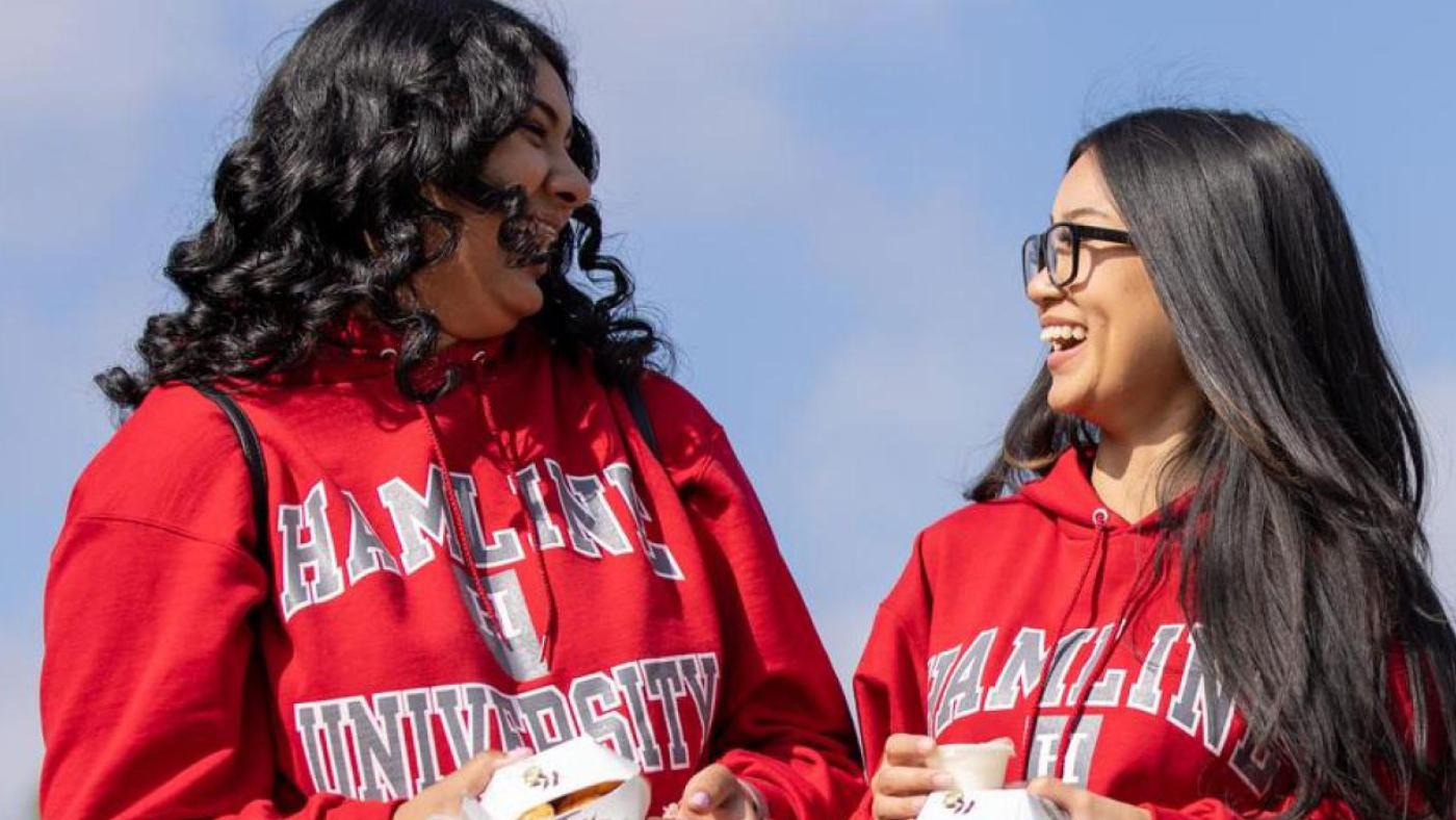 Two students carrying food and laughing during Hamline Homecoming and Alumni Weekend