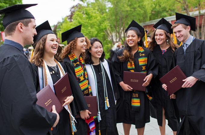 Photo of Hamline students at graduation dressed in cap and gown and holding their diplomas