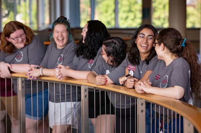 A group of new student mentors talking while leaning on a railing