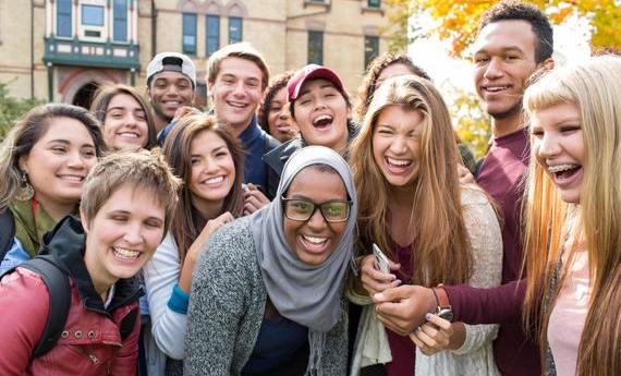 A group of smiling, laughing Hamline students gathered in front of Old Main and leaning together for the picture