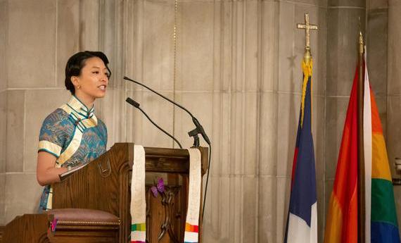 A person speaking at a podium during a Hamline Commencement with flags in the background