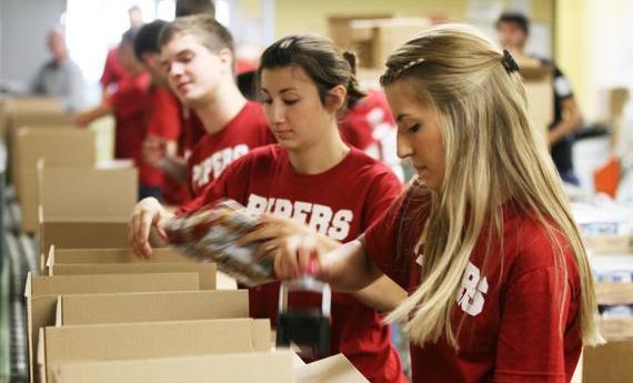 Three Hamline student wearing red "PIPERS" shirts taping cardboard boxes while volunteering