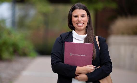 An MBA graduate student from Hamline's School of Business holding a folder and smiling at the camera