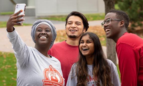 A group of four first-year Hamline students smiling and taking a selfie on campus