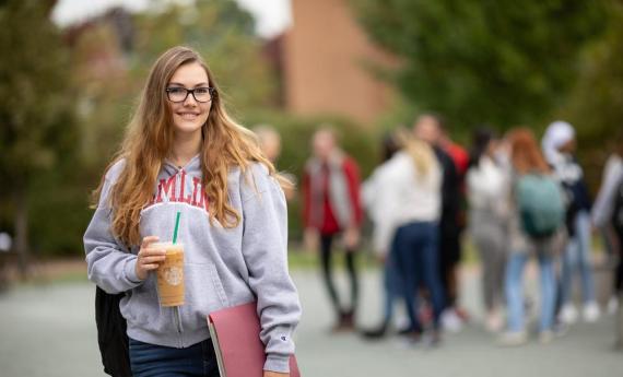 A new Hamline student smiling outside and other students in the background