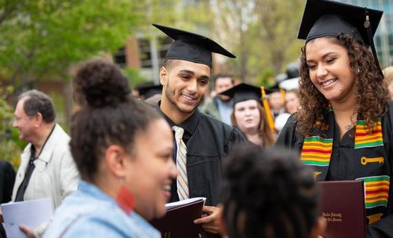 Hamline students wearing graduation robes holding their diplomas at commencement