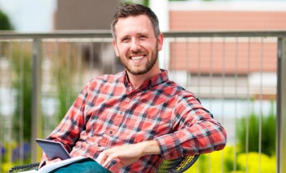 A Hamline graduate student sitting at a table outside on campus and smiling