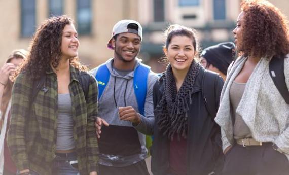 Four students standing outside side-by-side and smiling at each other