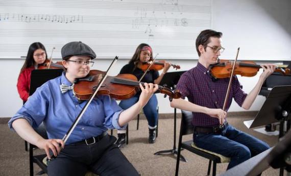 Four Hamline students in a music classroom playing violins and violas