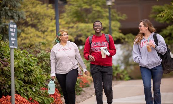 Three Hamline students walking and talking outside on campus in the fall