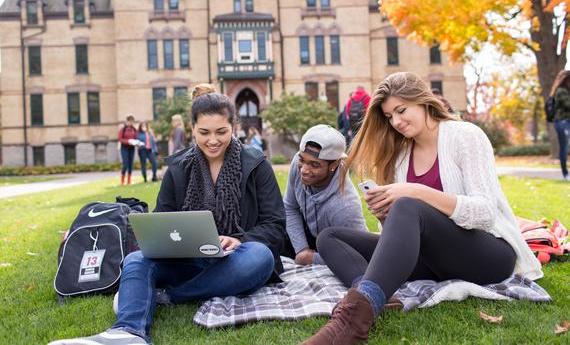 Three Hamline students sitting on a blanket on the grass outside Old Main