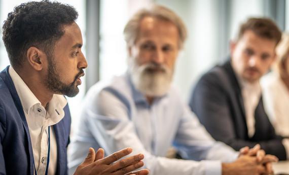 man sitting and speaking with others looking at him and listening