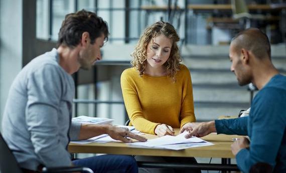 Three graduate students discussing around a table looking at a paper 