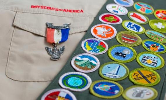 A close-up of a a Boy Scouts badge and a Girl Scout's sash full of patches