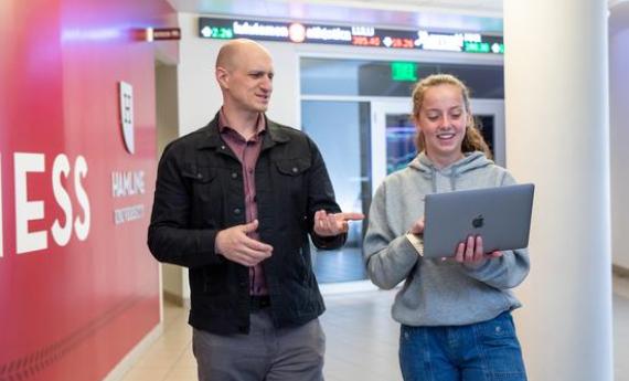 A Hamline student and professor walking side-by-side down a hallway talking