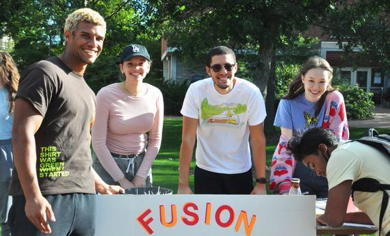 Students pose around a poster about their student organization, Fusion