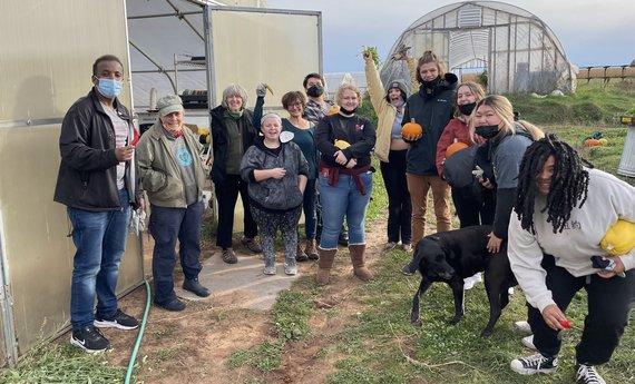 Hamline students and staff pose outside a greenhouse with peppers, pumpkins, and squash