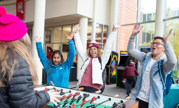 A few students cheer near a foosball table that they're playing on