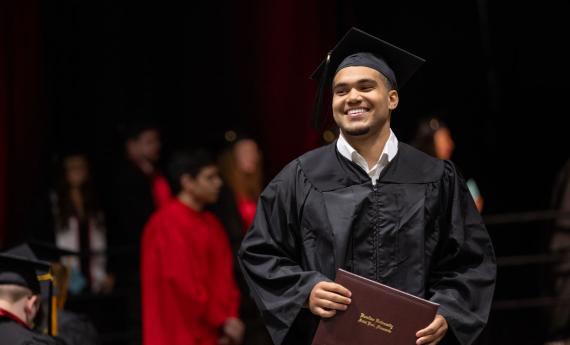 Graduate smiling and clutching diploma at 2026 Commencement