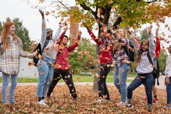 A group of students throwing fall leaves