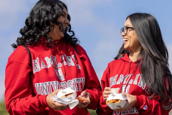 Two students carrying food and laughing during Hamline Homecoming and Alumni Weekend