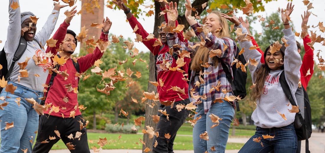 Students throwing fall leaves into the air on Hamline's campus