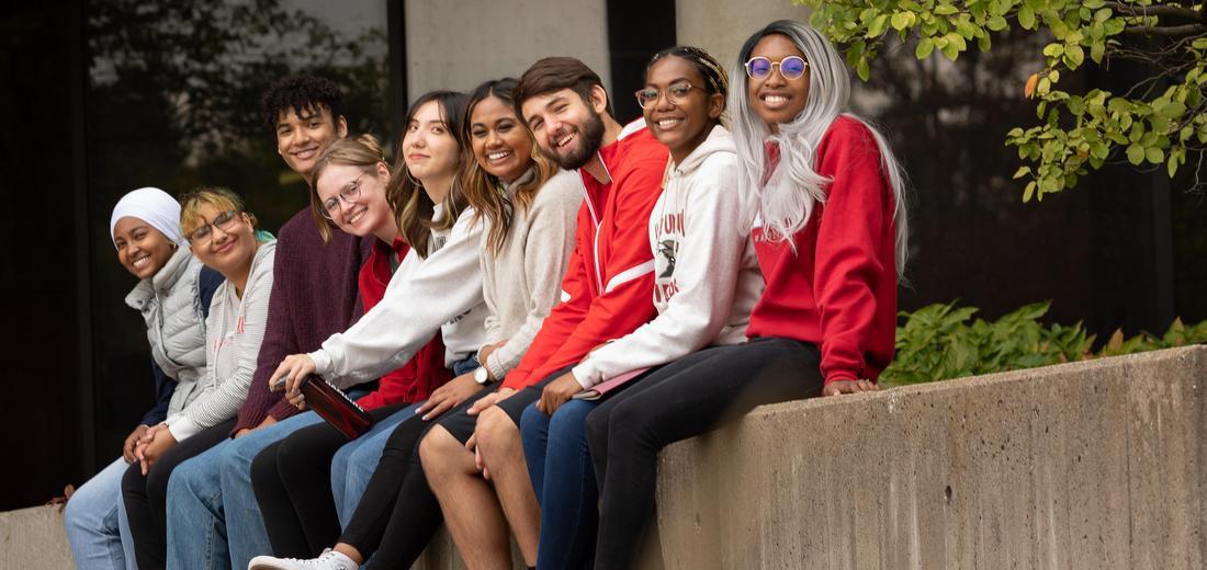 Photo of students sitting on campus and smiling at camera