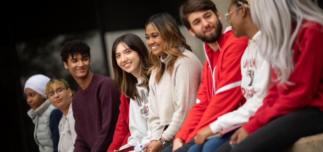 Diverse group of Hamline students sitting on a wall on campus