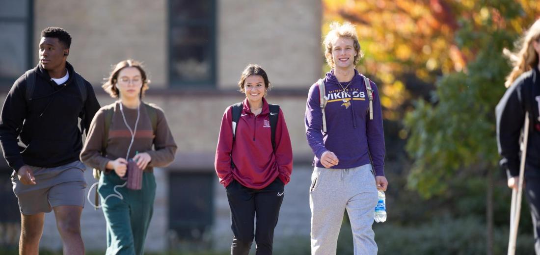Group of Hamline students walking in front of Old Main in fall