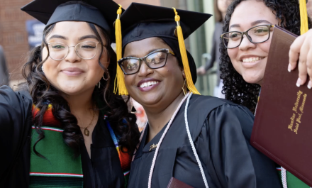 Three students taking a selfie while dressed in cap and gown at 2026 Commencement