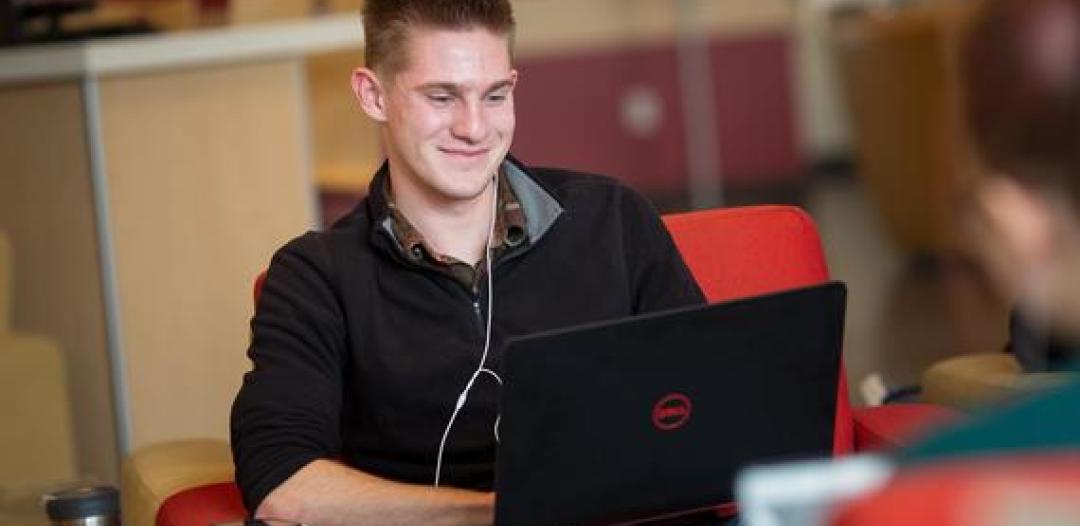 A Hamline student sitting with a laptop on their lap, smiling and typing