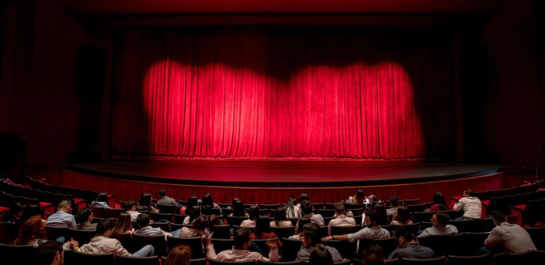 An audience looking at a theatre stage with a red curtain closed