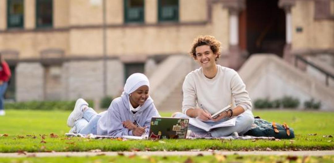 Two Hamline students sitting on the grass outside Old Main on campus
