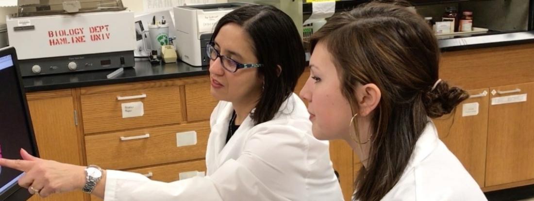 Two Hamline biology students in white coats looking at an image on a computer together