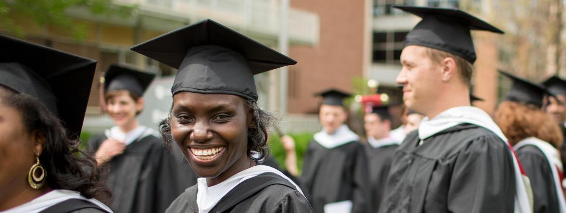 Hamline students in caps and gowns standing in line for Commencement, one smiling at the camera