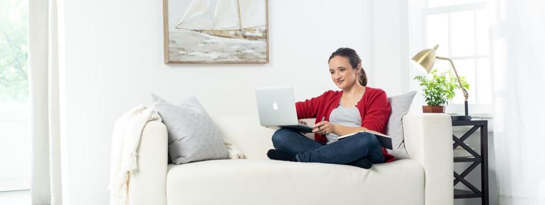 A person sitting on a couch smiling with their laptop on their lap