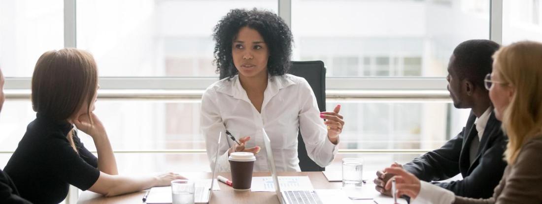 A person sitting at the head of a table speaking to four other people sitting around the table
