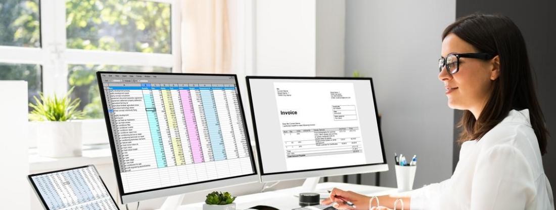 a person sitting at a desk with multiple monitors open to accounting spreadsheets