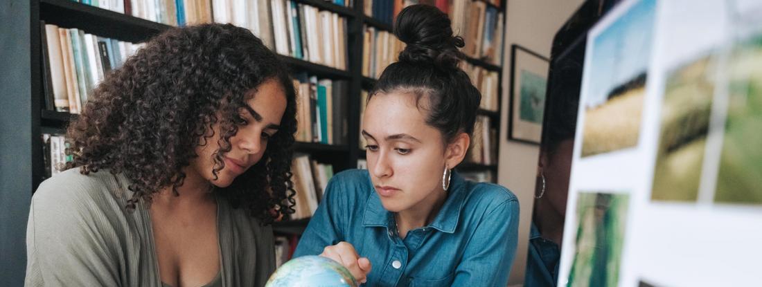 Two students looking at a globe in a library