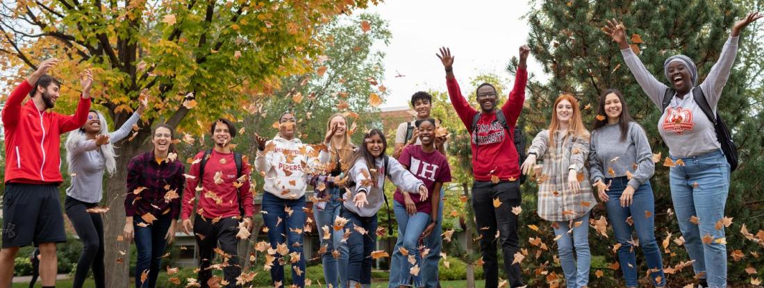 A group of Hamline students laughing outside and tossing fall leaves in the air