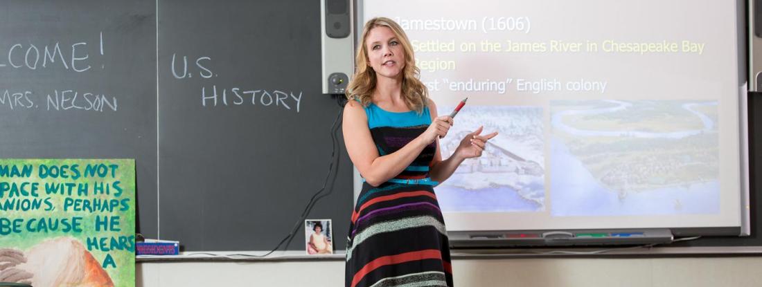 A teacher standing in a classroom with "US History" written on the chalkboard