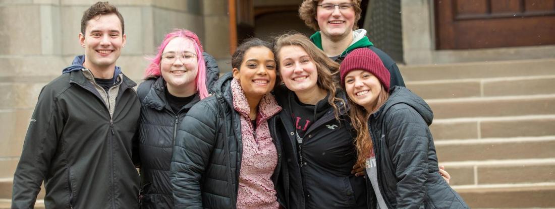 A group of Hamline students gathered outside a building on campus, smiling